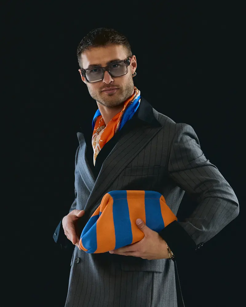 Dawid Krynicki in a grey suit with an orange and blue scarf and a striped bag