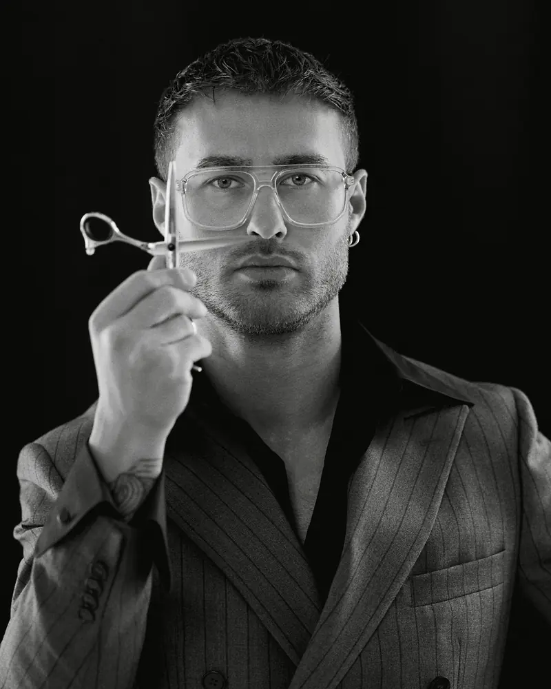 Dawid Krynicki holds hairdressing scissors up to his eye, black-and-white portrait