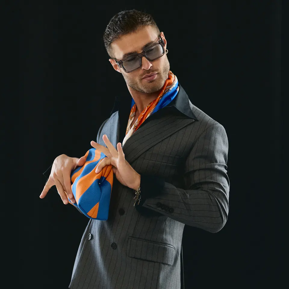 Dawid Krynicki in a grey suit, with a colourful scarf and a striped bag