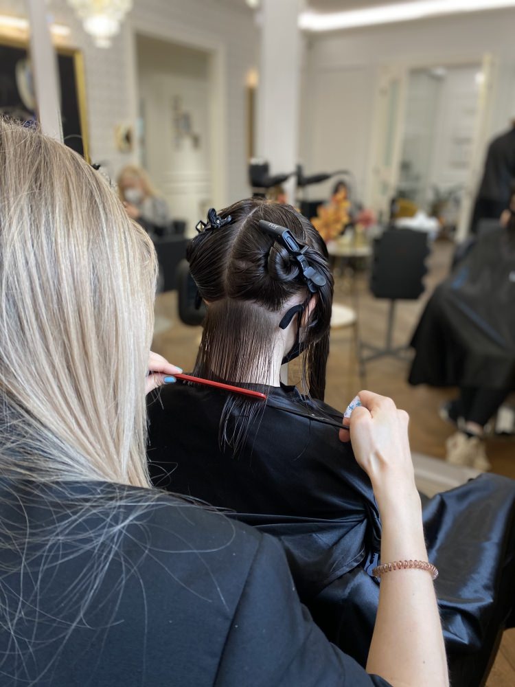 A stylist sections the client's hair before cutting, with the salon floor in the background